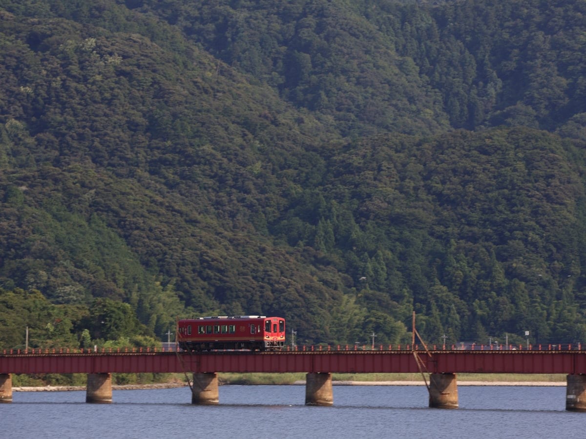 Red train crosses a bridge over blue water.