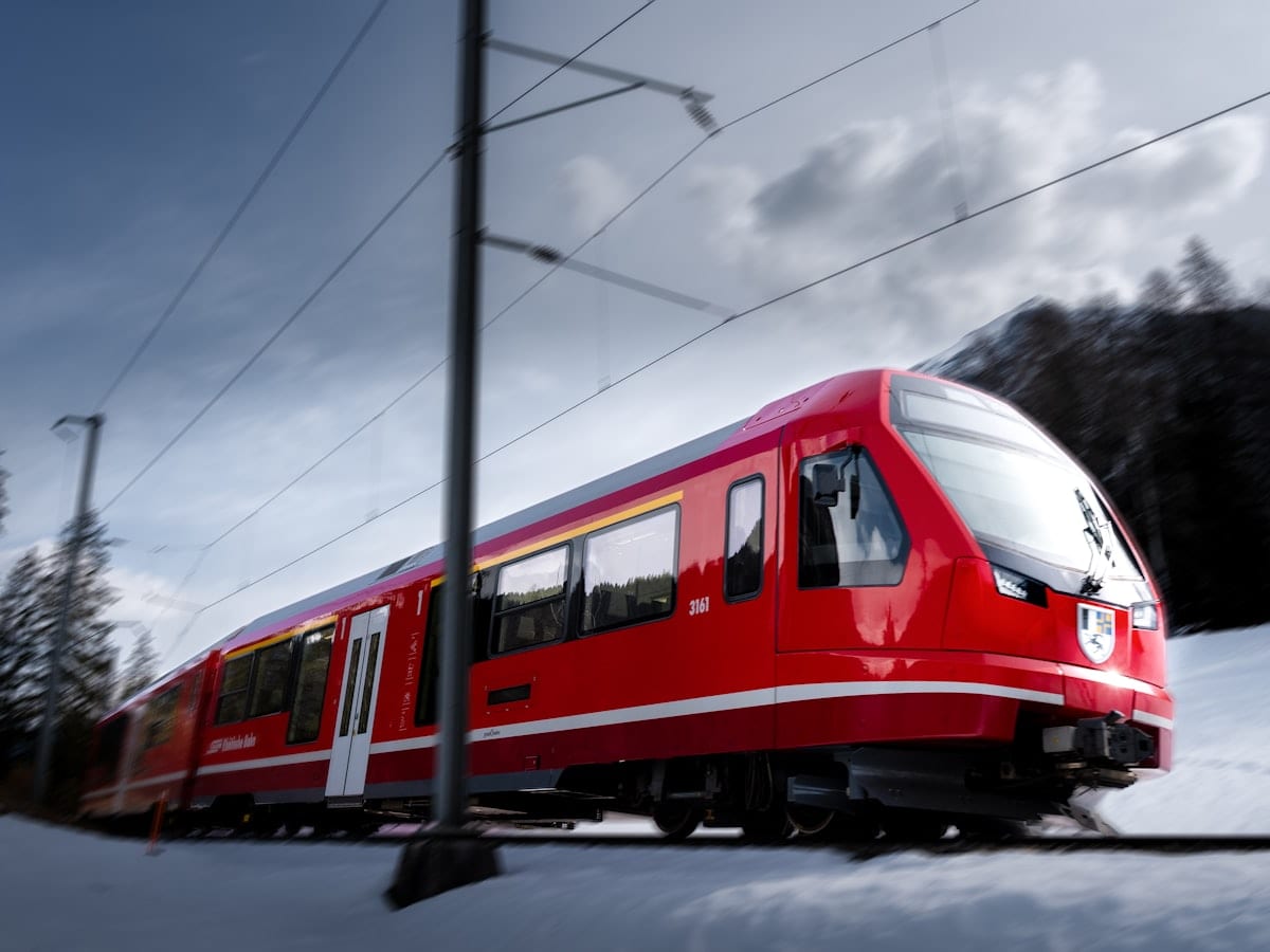 Red train on tracks in a snowy mountain landscape.