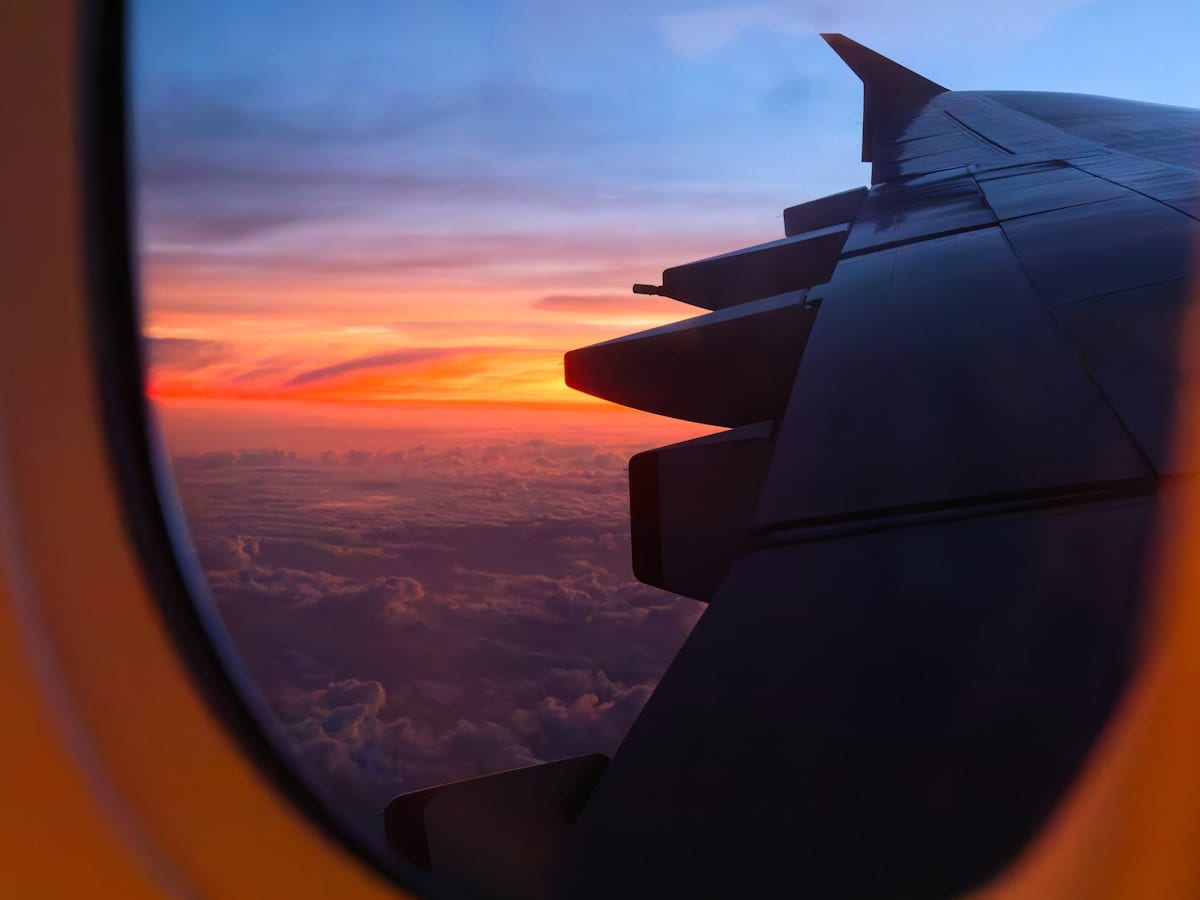 Airplane wing silhouetted against a colorful sunset sky from window.