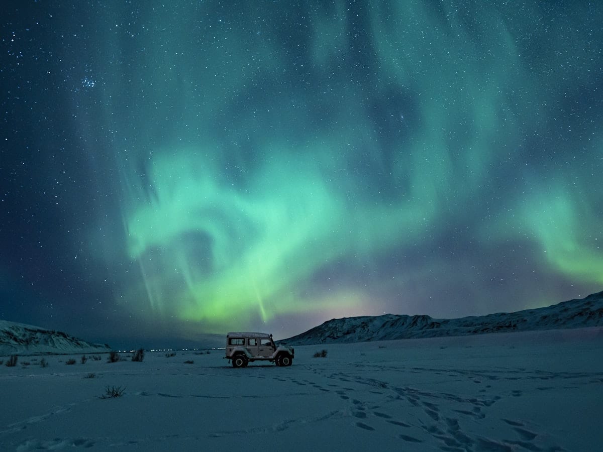 black suv on snow covered field under green aurora lights