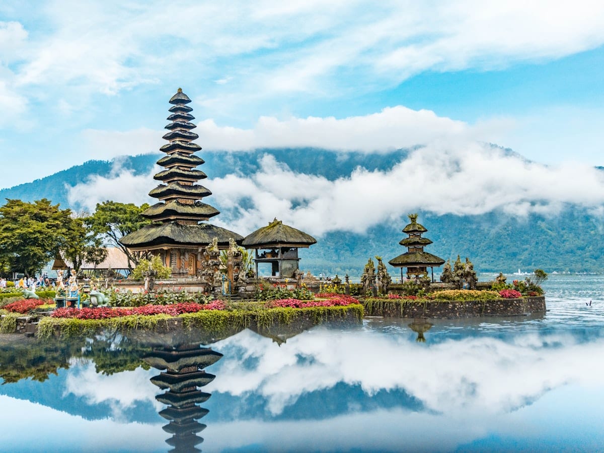 brown and green temple near body of water under blue and white cloudy sky during daytime