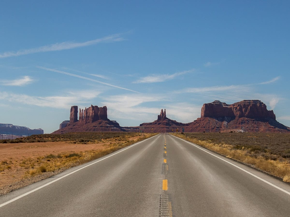 gray concrete road between brown mountains under blue sky during daytime